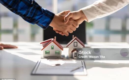 Global buyers shake hands over a real estate contract with model houses, symbolizing a property deal.
