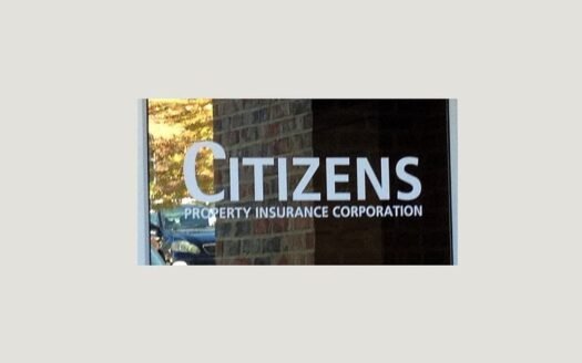 Sign for Citizens Property Insurance Corporation on a window in Florida. Brick wall and reflection of trees visible.